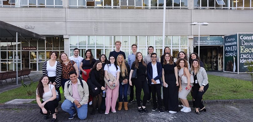 Fotografia de um grupo de jovens, entre homens e mulheres, posando sorrindo em frente à Central ...