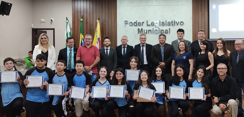 Estudantes de Pitanga (PR) são empossados pelo Projeto Parlamento Jovem Na imagem observam-se 11 jovens abaixados com uniformes escolares azul-claros segurando diplomas...