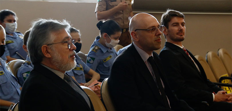 Fotografia de um grupo de pessoas assistindo ao julgamento simulado. Em destaque, aparecem três ...