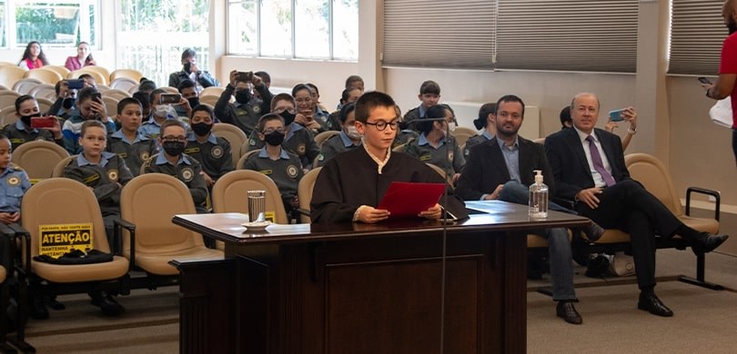 Fotografia da sala de sessões do TRE-PR com estudantes, autoridades, servidoras e servidores dur...