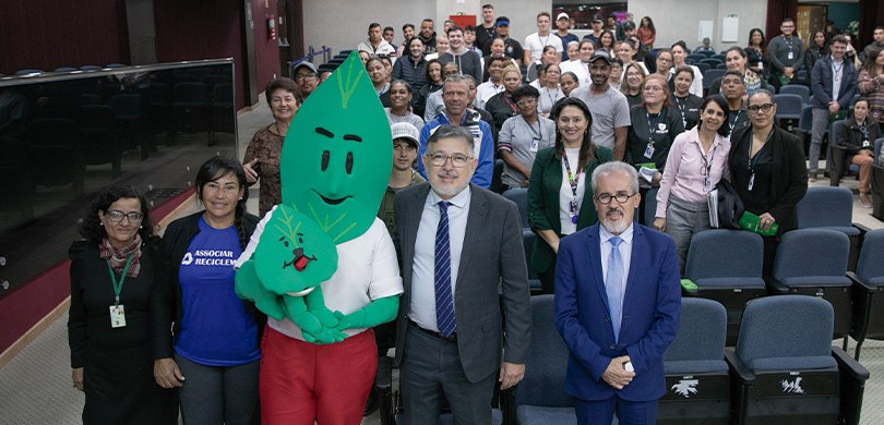 Fotografia de diversas pessoas, entre homens e mulheres, posando sorrindo na plateia de um audit...