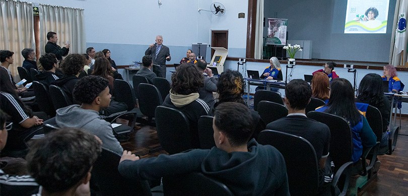 Fotografia do desembargador Sigurd Roberto Bengtsson de terno cinza falando diante de alunas e a...