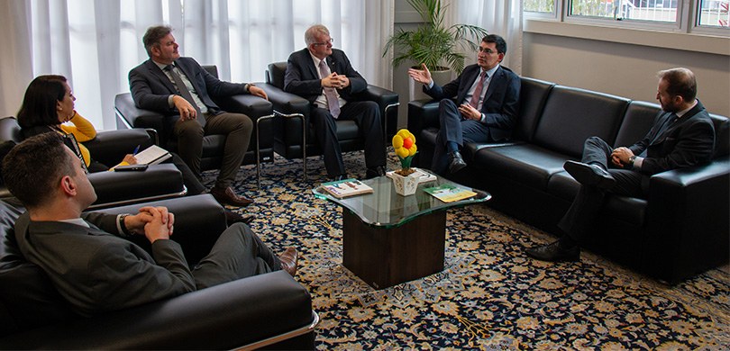 Ex-membro da Corte Constitucional da Colômbia enaltece transparência e organização do processo eleitoral Cinco homens vestindo ternos e uma mulher, de blusa amarela, sentam-se em poltronas pretas que e...