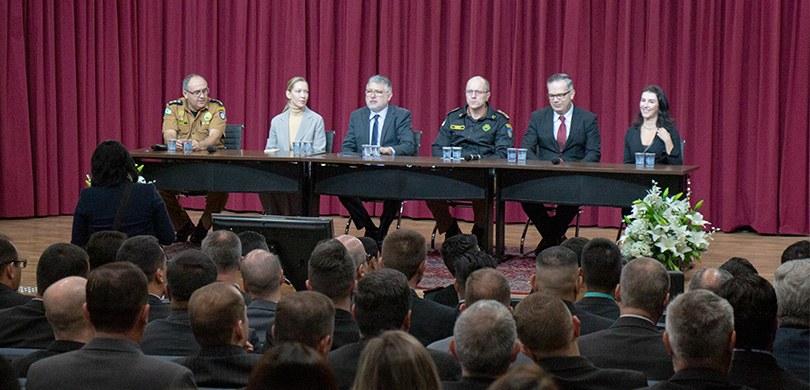 Formatura do curso de inteligência da Polícia Militar acontece no TRE-PR Fotografia da mesa de autoridades em um auditório. Sentados à mesa estão duas mulheres e quatro ...