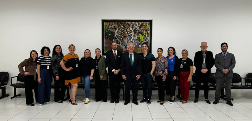 Fotografia de diversas pessoas, entre homens e mulheres, posando sorrindo. A sala tem paredes e ...