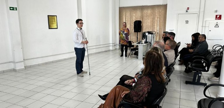 Fórum Eleitoral de Ponta Grossa inaugura sala calma e realiza capacitação para atendentes Fotografia em que se vê, do lado esquerdo, um homem segurando uma bengala e falando ao público, ...