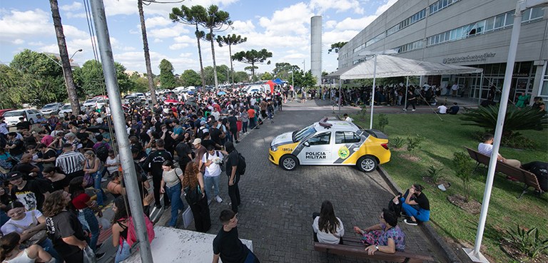 Foto do pátio interno do Fórum Eleitoral de Curitiba. Do lado esquerdo, veem-se muitas pessoas e...