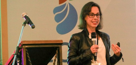Fotografia de seis pessoas, quatro mulheres e dois homens, posando sorrindo em frente a um palc...