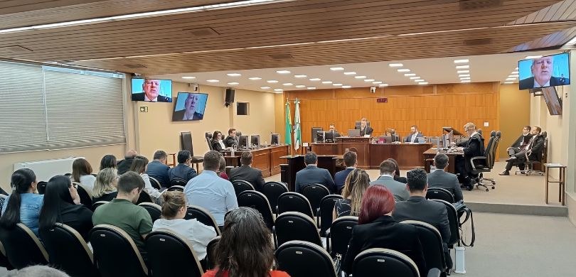 Gestão 2024-2025 conduz última sessão de julgamento da Corte do TRE-PR Fotografia da sala de sessões do TRE-PR ocupada por diversas pessoas sentadas em poltronas escur...