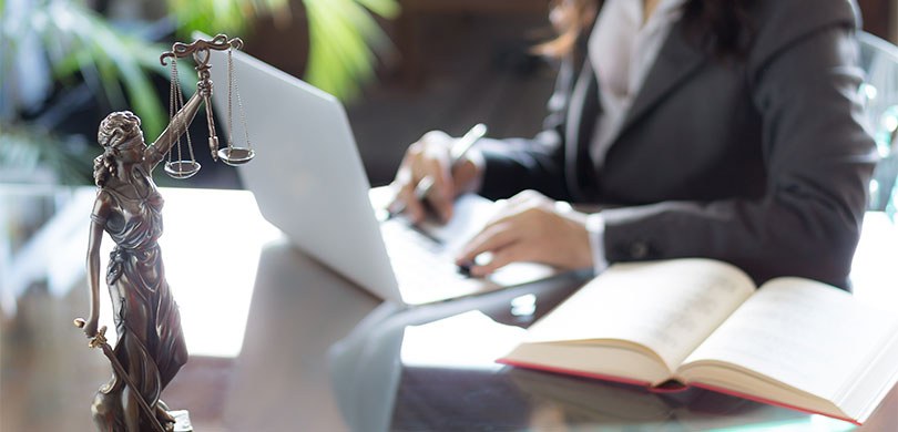 Fotografia de uma mulher de terno e cabelo castanho mexendo em um notebook, sobre uma mesa de vi...