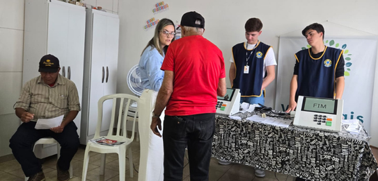 Fotografia de cinco pessoas, quatro homens e uma mulher, em uma sala clara. Dois rapazes com col...