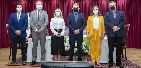 Fotografia de um grupo de pessoas em pé em cima de um palco. Elas estão sobre um tapete vermelho...