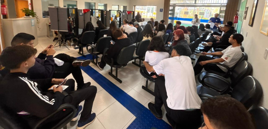 Fotografia de uma mulher em pé palestrando para jovens uniformizados em uma sala de aula com par...