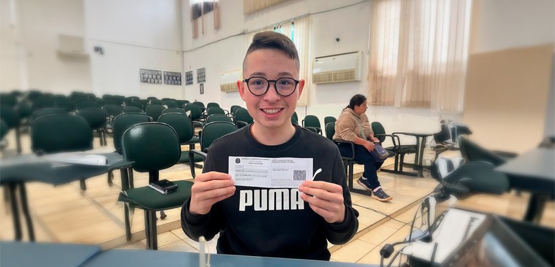 Fotografia do jovem Eduardo Smolak de Abreu sorrindo e segurando a primeira via do Título de Ele...