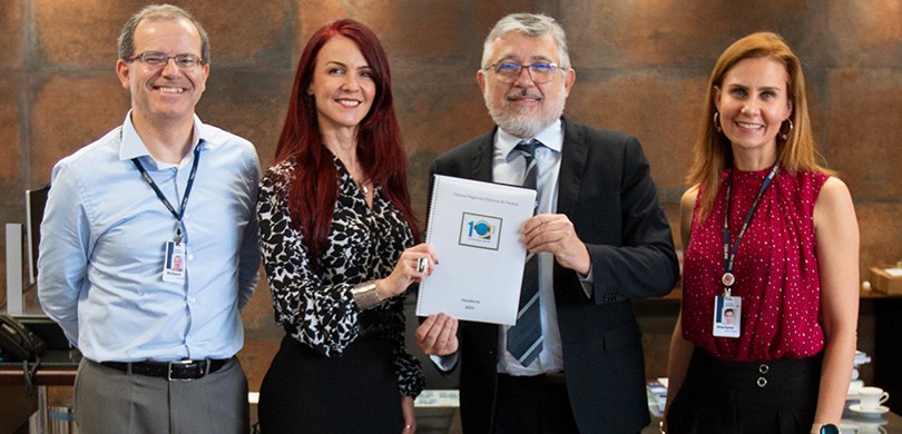 Fotografia de quatro pessoas, duas mulheres e dois homens, posando para foto. A mulher e o homem...