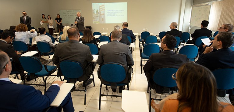 Juízes eleitorais participam da segunda aula presencial do curso de aperfeiçoamento 2 Fotografia de diversas pessoas, entre homens e mulheres, sentados em carteiras escolares em uma ...