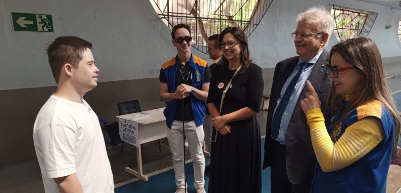 Fotografia em que aparecem oito pessoas posando em um guichê de atendimento, entre as quais está...