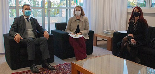 Fotografia de três pessoas sentadas em um gabinete, sendo duas mulheres, à direita, e um homem, ...