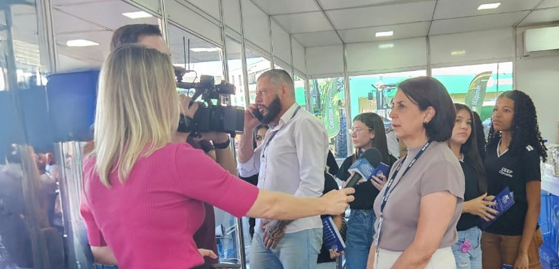 Foto de uma repórter e um cameraman entrevistando a diretora-geral Solange Maria Vieira. Ao fund...