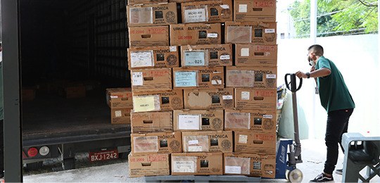 Um homem arrasta uma pilha de caixas de papelão com urnas dentro. Atrás está um caminhão aberto.