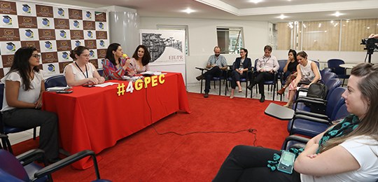 “Justiça Eleitoral e ONU Mulheres” é tema do Grupo de Pesquisas em Direito Eleitoral e Ciência Política Fotografia de uma sala com tapete vermelho. À esquerda, há uma mesa com uma toalha vermelha e qu...