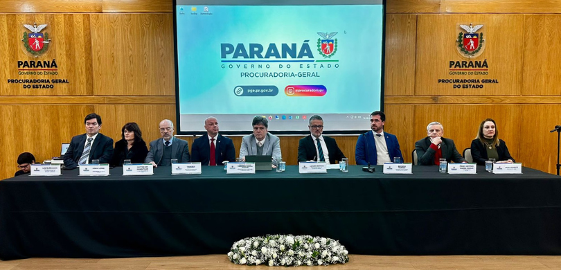 Justiça Eleitoral participa da celebração do 79° aniversário da Procuradoria-Geral do Estado do Paraná (PGE-PR) Fotografia de uma mesa de autoridades composta por duas mulheres e sete homens. Sobre a mesa há ...
