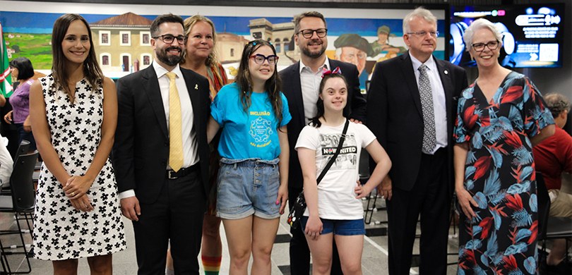 Foto em que aparecem oito pessoas adultas, três homens vestindo ternos e cinco mulheres, três us...