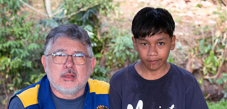 O presidente do TRE-PR, um homem branco, com barba e óculos de grau, do lado de um menino indige...