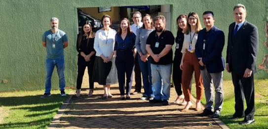 Fotografia de 11 pessoas, entre homens e mulheres, posando sorrindo em frente ao Fórum Eleitoral...