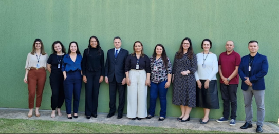 Fotografia de 11 pessoas, entre homens e mulheres, posando sorrindo em frente ao Fórum Eleitoral...