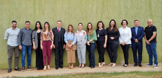 Fotografia de 11 pessoas, entre homens e mulheres, posando sorrindo em frente ao Fórum Eleitoral...