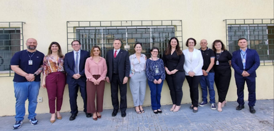 Fotografia de 11 pessoas, entre homens e mulheres, posando sorrindo em frente ao Fórum Eleitoral...