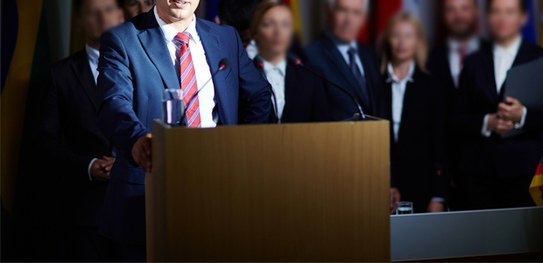 Lei que traz de volta a propaganda partidária tem novidades Foto de um homem de terno e gravata falando em um púlpito. Ao fundo há algumas pessoas com os ro...