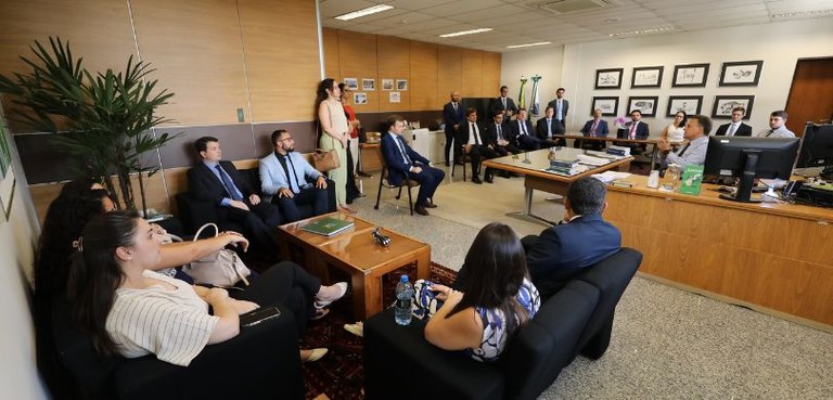 Magistrados participam do terceiro dia do curso de formação promovido pela EJE-PR 3 Fotografia de homens e mulheres em uma sala com paredes trabalhadas em madeira e carpete cinza. ...