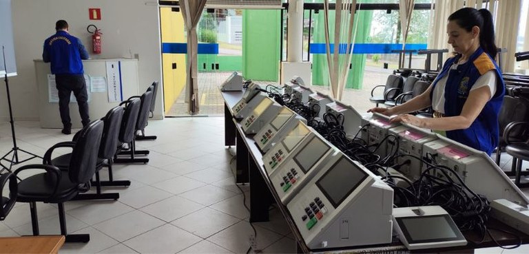 Fotografia em que se observa, em um salão com piso claro, uma mulher vestindo colete da Justiça ...