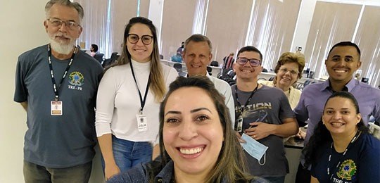 Grupo de oito pessoas, sendo quatro mulheres e quatro homens, posando sorrindo para uma selfie. ...