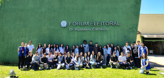 Fotografia de uma mulher em pé palestrando para jovens uniformizados em uma sala de aula com par...