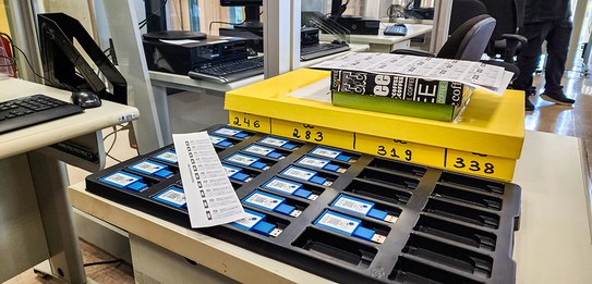 Fotografia de uma série de guichês de atendimento. Há um homem de terno e gravata em pé observan...