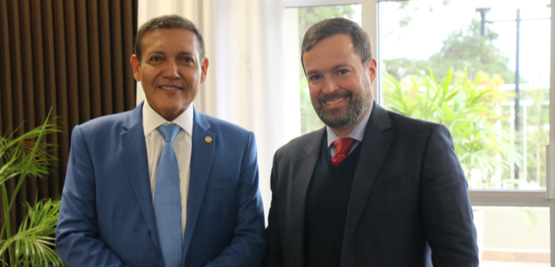 Fotografia de dois homens, de pele clara e cabelos escuros, posicionados lado a lado em pose par...