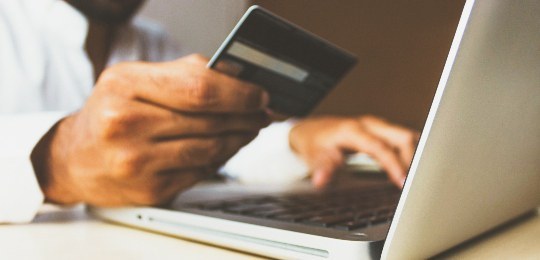 Imagem de um homem mexendo em um notebook e segurando um cartão de banco na mão