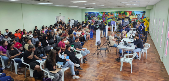 Fotografia que retrata o atendimento eleitoral em uma sala de aula adaptada. Dois cidadãos são a...