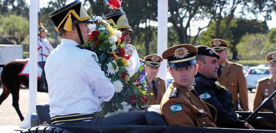 Na foto, policiais militares dirigem um carro oficial, sobre o qual homens em trajes especiais c...
