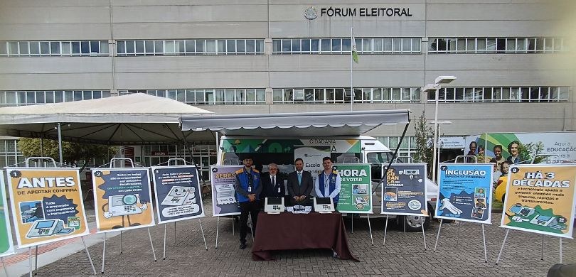 Fotografia de quatro homens posando sorrindo em frente ao Fórum Eleitoral de Curitiba. Dois home...
