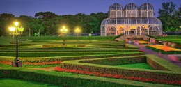 A fotografia é do Jardim Botânico de Curitiba. Está anoitecendo e mostra a estufa do local no la...