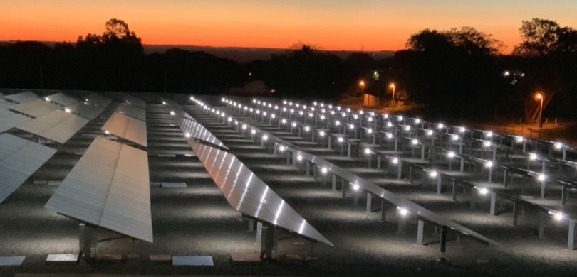 Na fotografia, há vários painéis fotovoltaicos uns ao lado dos outros.  Ao fundo, no horizonte, ...