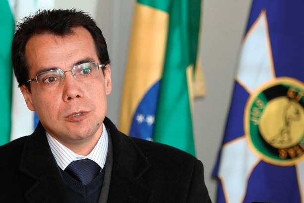 Nota de pesar pelo falecimento do procurador da República Alessandro José Fernandes de Oliveira Fotografia de um senhor de óculos, de terno e gravata preto, com uma bandeira desfocada ao funso