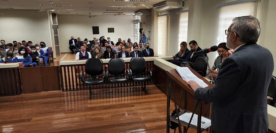 Um homem, que veste terno, está falando em um púlpito enquanto uma plateia o assiste.