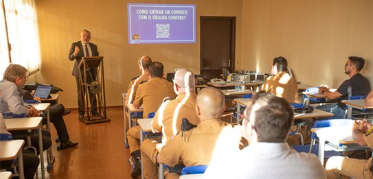 Um homem, que veste terno, está falando em um púlpito enquanto uma plateia o assiste.