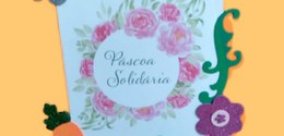 Foto de um papel impresso escrito Páscoa Solidária, com flores ao seu redor e decorações de flor...