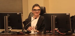 Fotografia da juíza Vanessa Jamus Marchi sentada na Corte do TRE-PR, posicionada entre dois moni...
